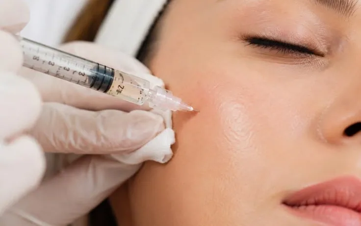 A gloved hand gives a fine injection in the cheek