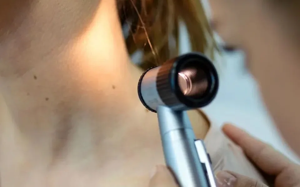 A doctor checks moles on a patient's neck with a dermatoscope
